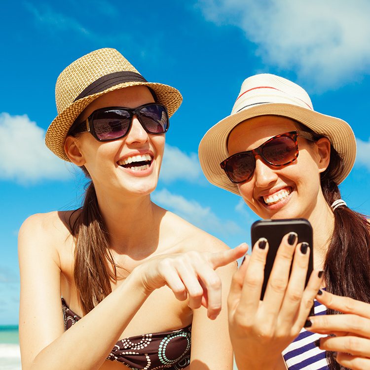 Pretty girls using smart phone on the beach. Summer holiday, tec